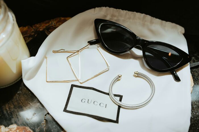 Sunglasses and jewelry on a Gucci pouch, embodying the 'pretend rich' aesthetic.