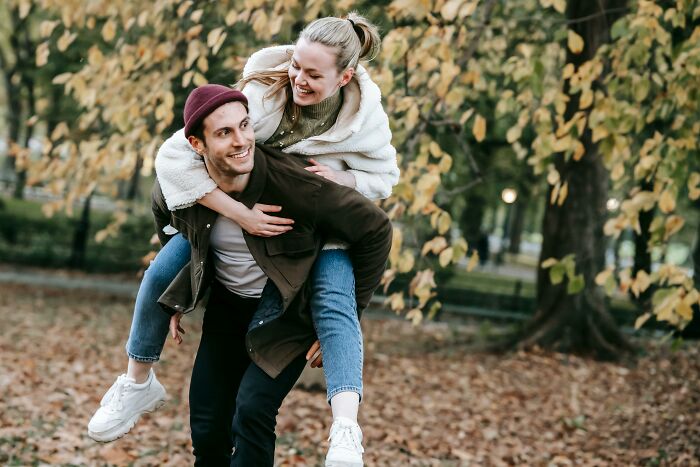 Man giving a woman a piggyback ride in a park, smiling and enjoying a playful moment together.