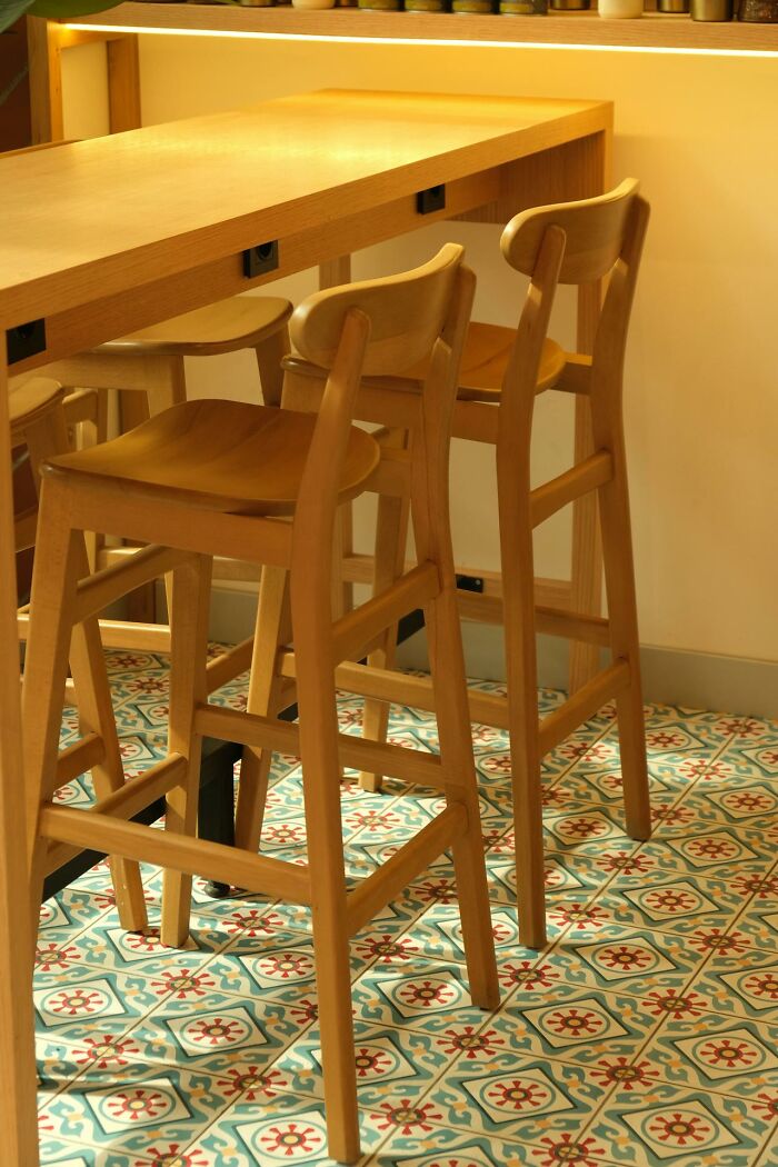 Modern wooden bar stools at a tall counter on patterned tiles, blending aesthetic appeal with limited practicality.