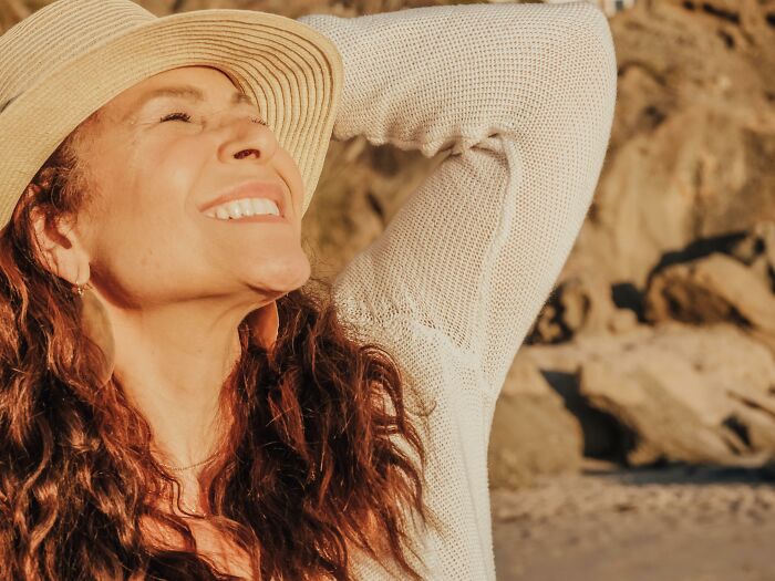 Woman joyfully smiling in the sun at the beach, wearing a hat, a reason to stop going to church discussed in viral thread.