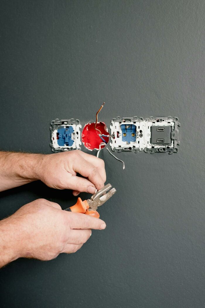 Electrician using pliers to work on wiring in a wall socket.