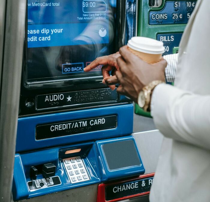 Person at a metro fare machine with card and coffee, potentially finding a loophole.