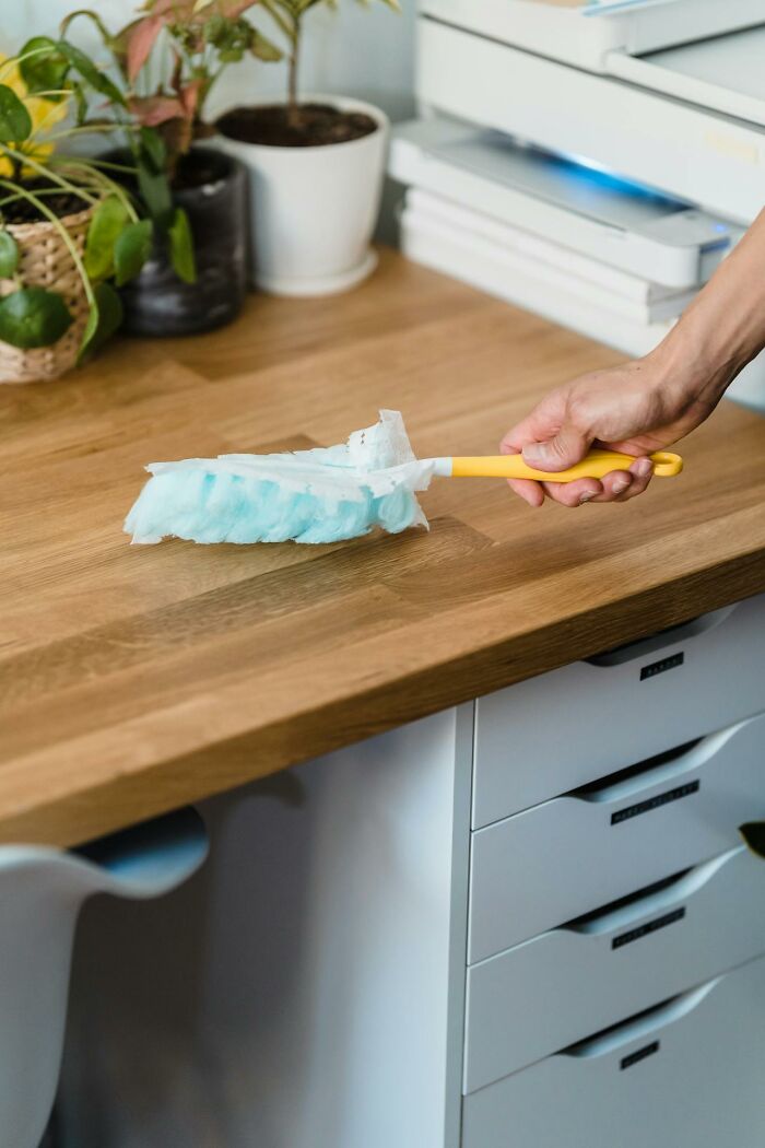 Hand dusting a wooden countertop, emphasizing strict cleaning rules.