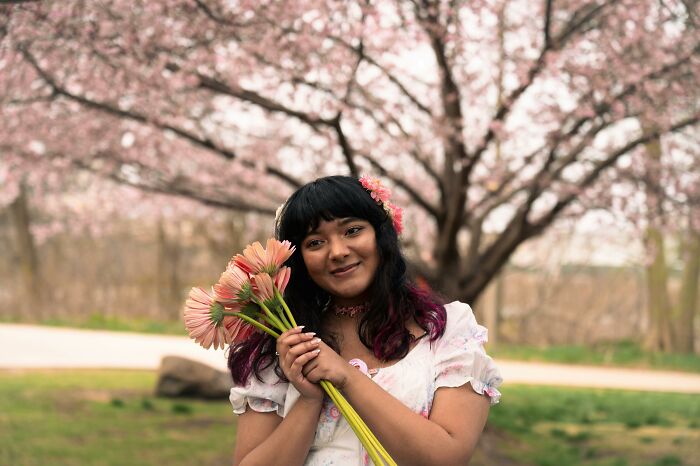 Smiling person holding flowers under blooming tree, symbolizing positivity despite past bully incidents.