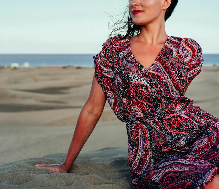Woman in a patterned dress sitting on sand by the sea, representing Americans who’ve moved abroad.