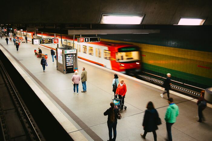 People at a subway station platform with a red train passing by, capturing everyday transit moments.