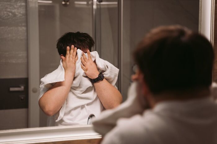 Person drying face with towel in bathroom mirror, focusing on hygiene tips.