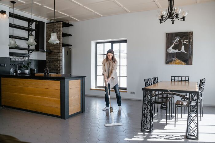 Person mopping a modern kitchen floor, exemplifying strict cleaning rules in a sunlit room.