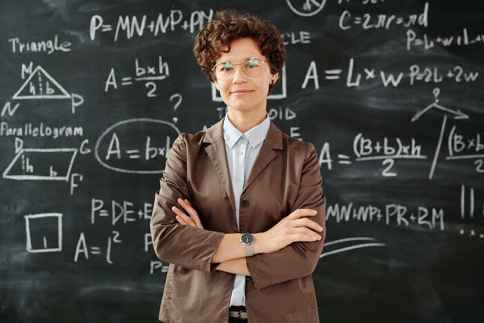 Woman sharing red pill stories in front of a chalkboard filled with mathematical formulas and diagrams, confident and thoughtful.