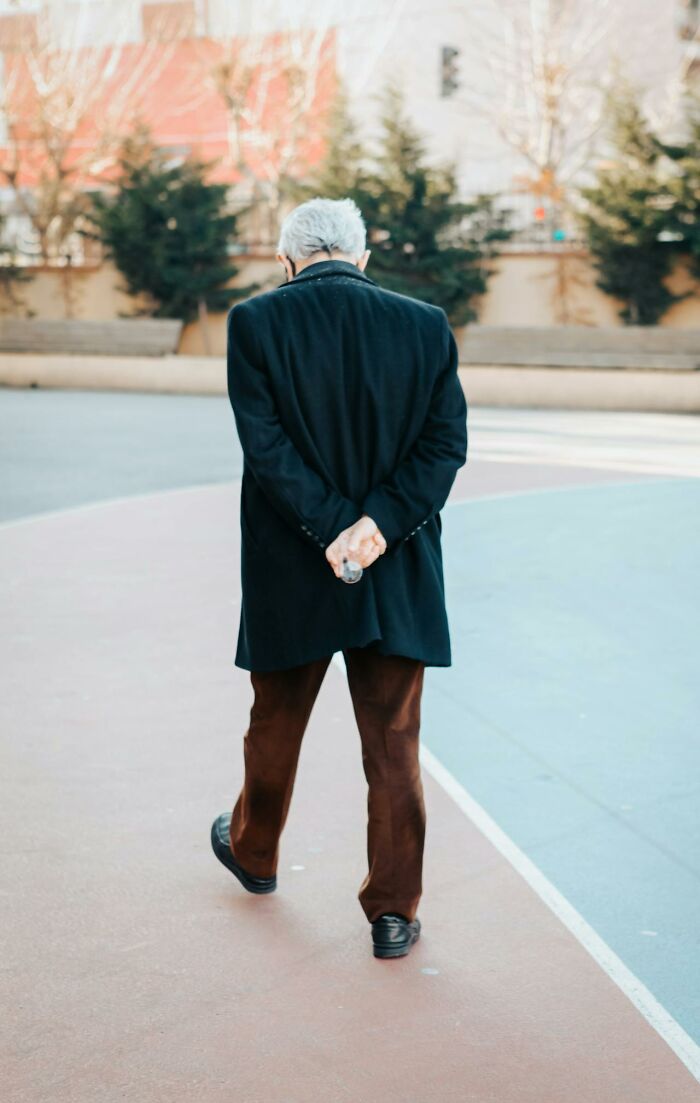 Elderly man walking alone outdoors with hands behind back, symbolizing awareness and reflection on obvious things.