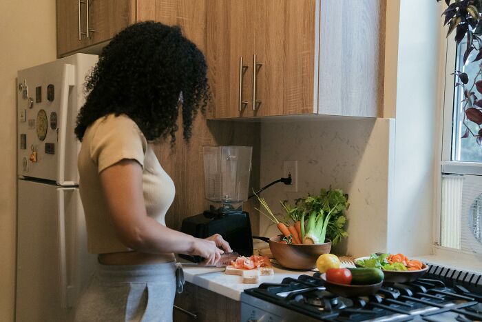 Woman in kitchen preparing vegetables beside a blender, exploring girlfriend dynamics insights.