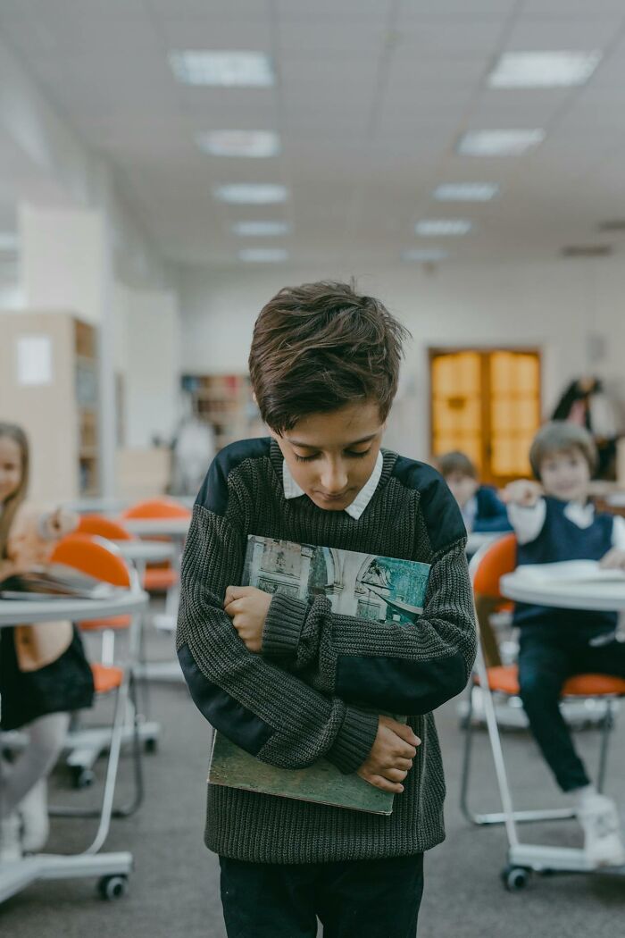 Child in a classroom hugging a book, illustrating a hidden traumatic experience.