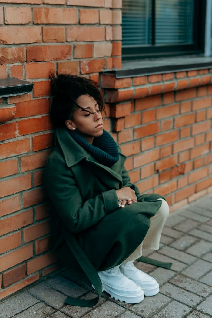 Person in a green coat sitting against a brick wall, reflecting quietly, related to first responders' memorable moments.