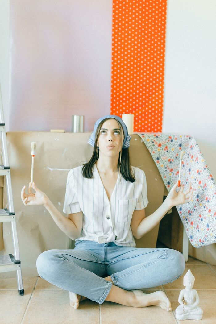 Woman meditates with paintbrushes in hand, surrounded by home decor elements.