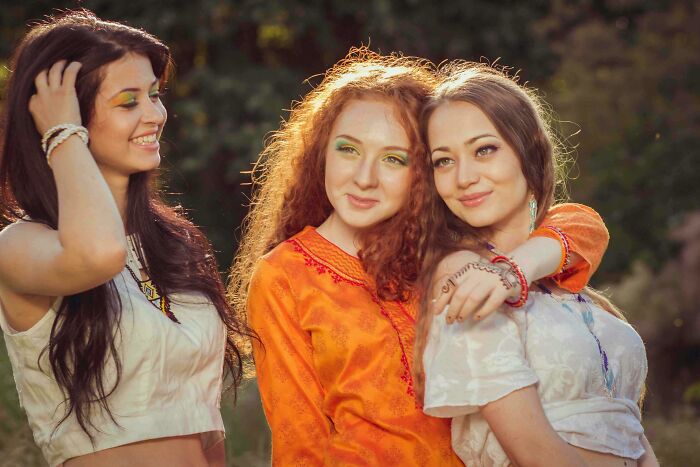 Three women smiling together in bright clothing, embodying youthful habits.