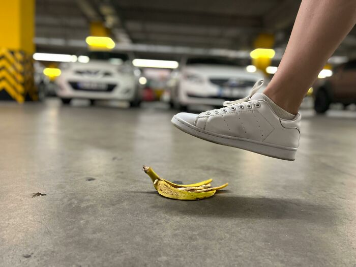 White shoe about to step on a banana peel in a parking garage, illustrating everyday danger.