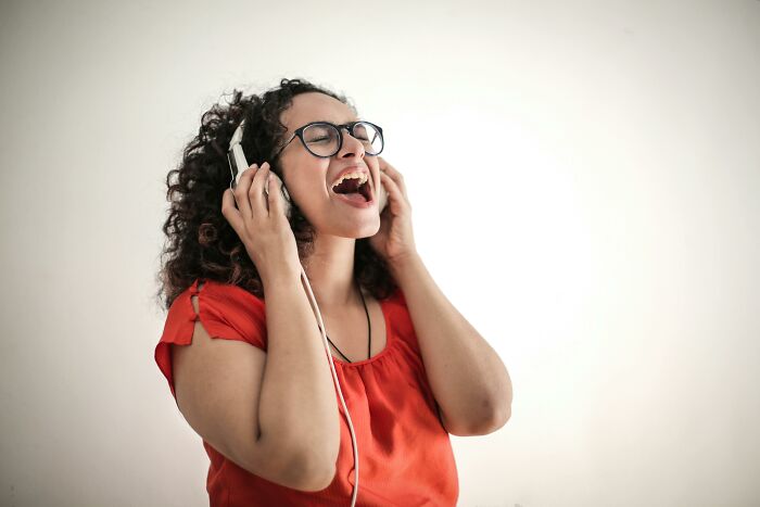 Woman in red shirt wearing headphones singing along, enjoying music and filling in song lines with missing words.