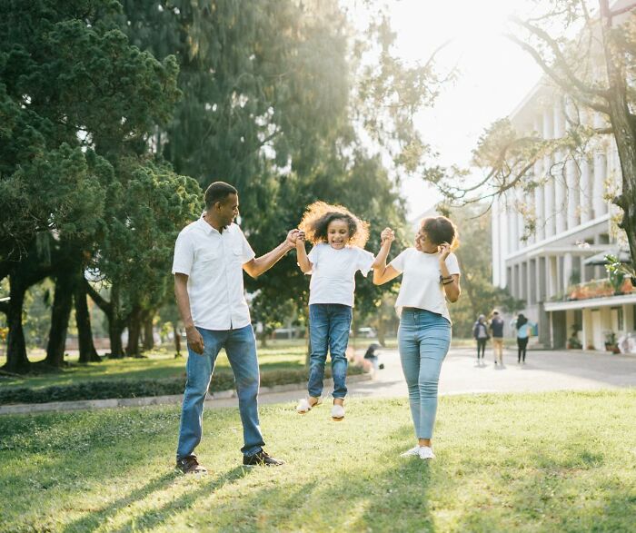 Family enjoying a sunny day at the park abroad, with parents lifting their child, highlighting Americans moving permanently.
