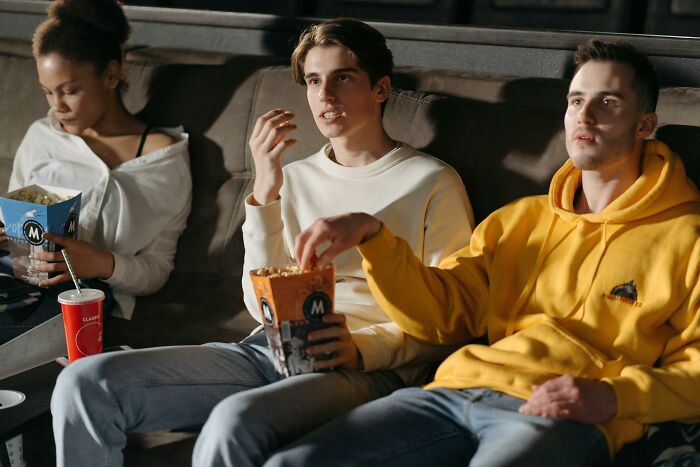 Three friends on a couch, one speaking confidently while eating popcorn, embodying absolute confidence.