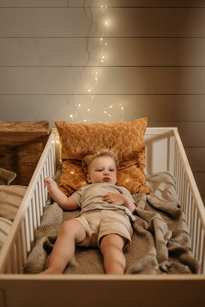 Toddler lying in a crib with cozy blankets and pillows, showcasing a peaceful moment in parenting.
