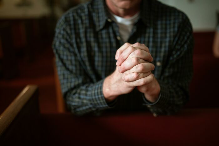 Man in a church pew clasping hands in prayer, representing reasons people stop attending church.