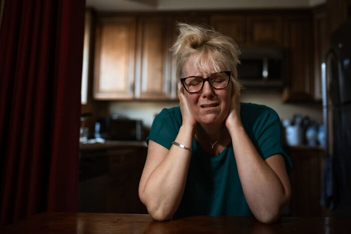 A distressed woman in glasses holding her head, illustrating emotional impact first responders experience after difficult calls.