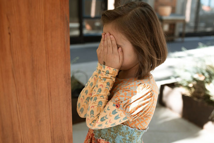 Child covering face with hands, feeling uncomfortable at an engagement setting.