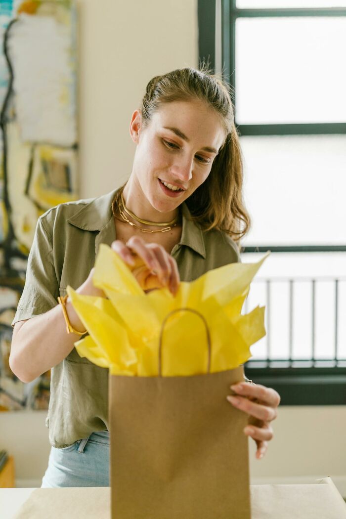 Woman opening a gift bag with yellow tissue paper, illustrating confusion in women's experiences.