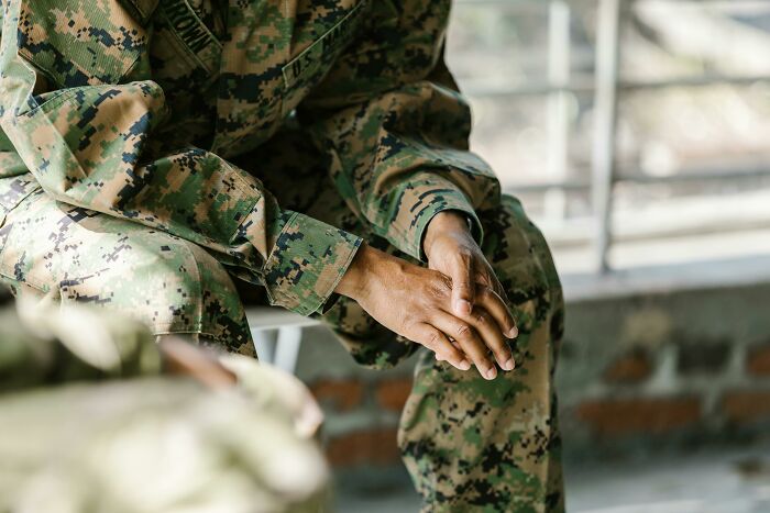 Close-up of soldier in camouflage uniform sitting with hands clasped, reflecting on a WWI recruit test question. Close-up of soldier in camouflage uniform sitting with hands clasped, reflecting on a WWI recruit test question.