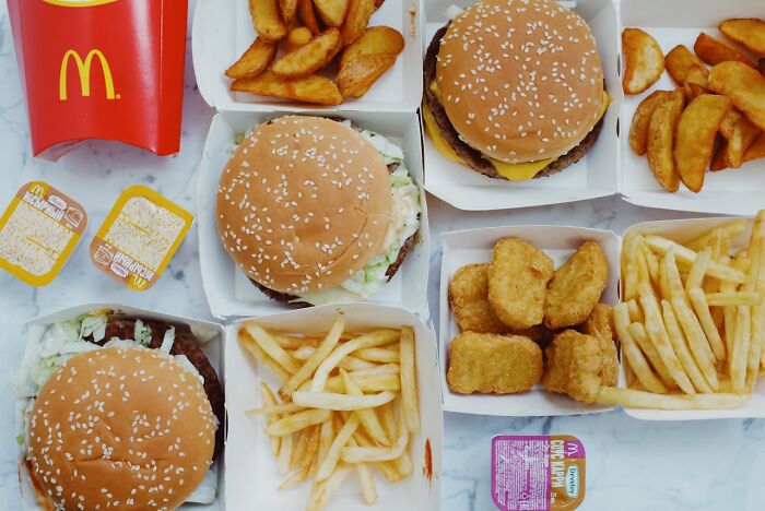 Fast food restaurant food including burgers, fries, and nuggets displayed in takeaway packaging on a marble surface.