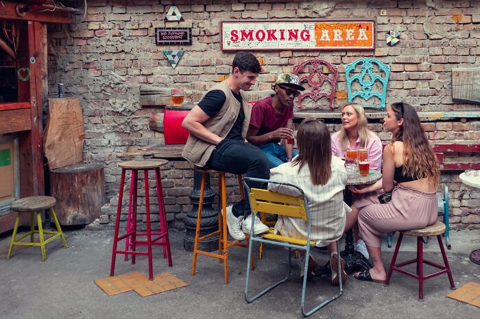 People enjoying drinks and conversation in an outdoor smoking area with colorful stools and decor.