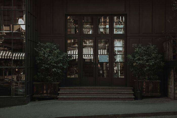 Dark building entrance with glass doors and potted plants, capturing a mysterious atmosphere.