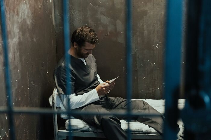 Man sitting on a prison bed looking at a photo, reflecting on why guys slept with a married woman in a dim cell.