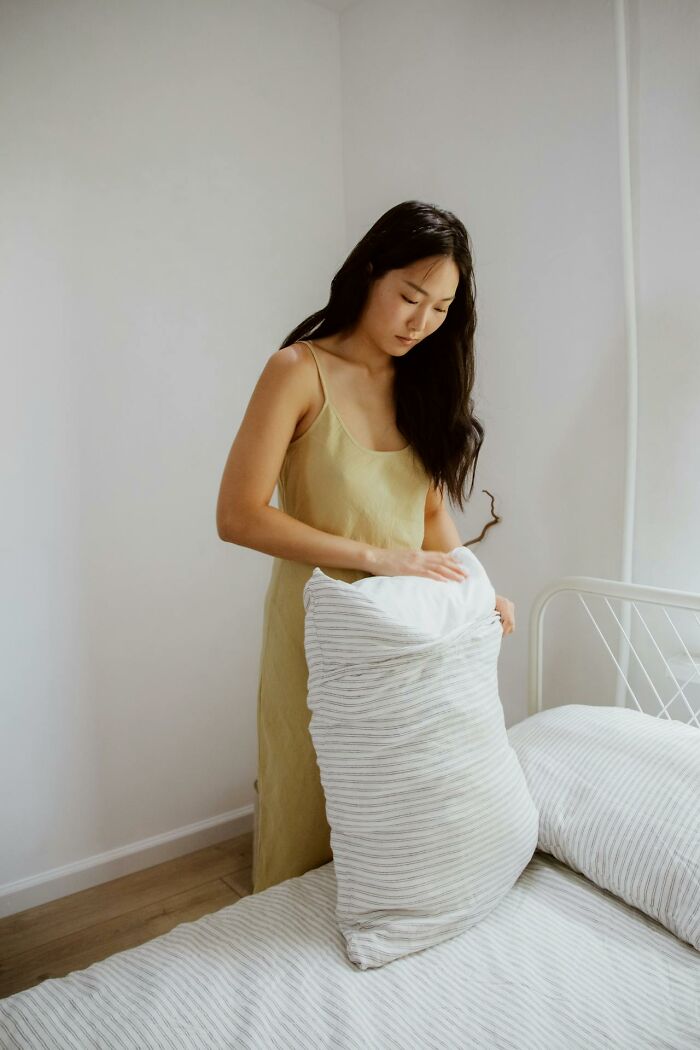 "Person fluffing a pillow, demonstrating their strict cleaning rules in a tidy bedroom."