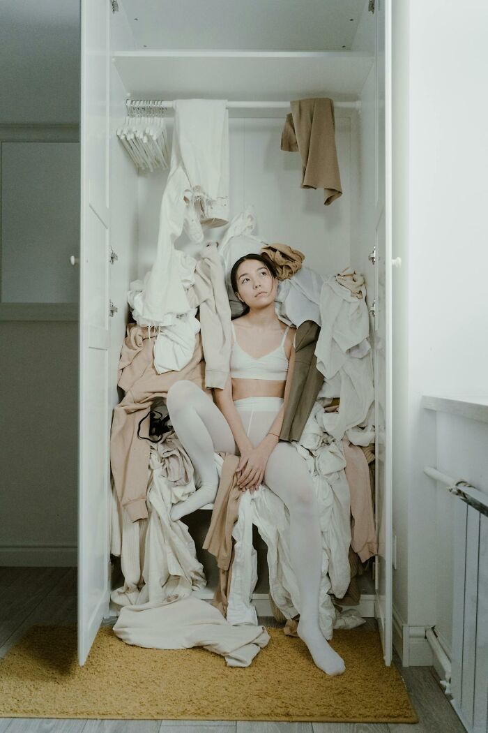 Woman surrounded by clothes in a closet, contemplating common confusions between women and men.