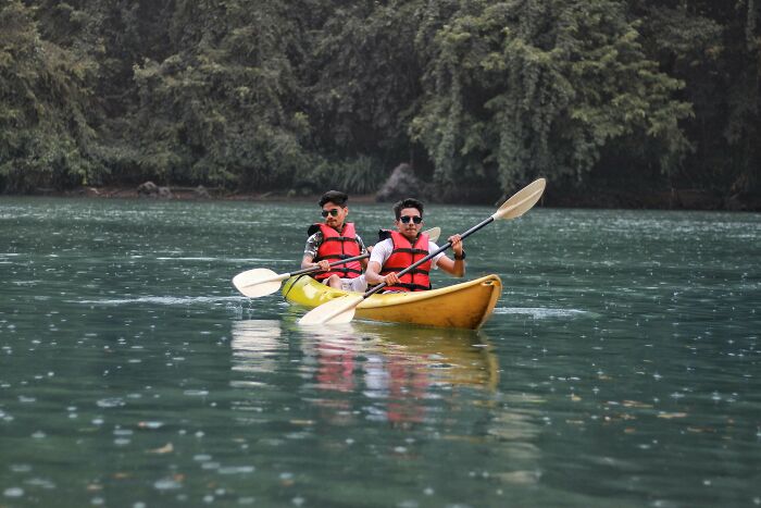 Two people kayaking on a calm river, wearing life vests; an activity that seems harmless but can be dangerous.