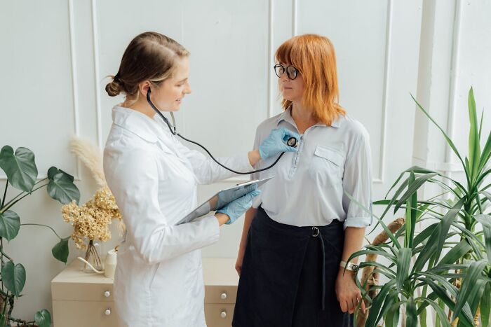 Female doctor using stethoscope to examine woman patient in clinic highlighting unfair treatment from doctors.