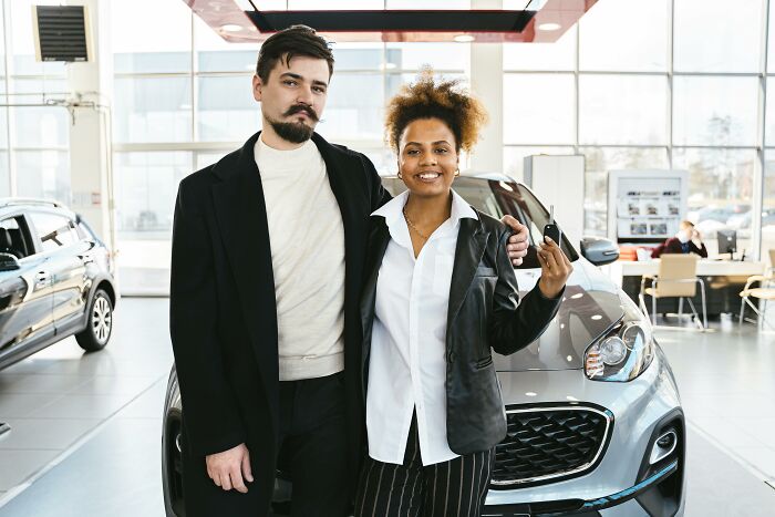 Couple in a car dealership, smiling and holding car keys, illustrating immature habits of adults in their 30s.