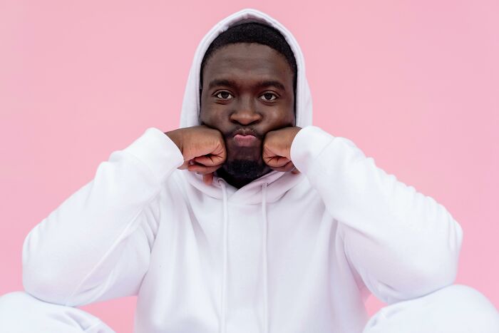 Man in a white hoodie making a playful face against a pink background, displaying immature habits.
