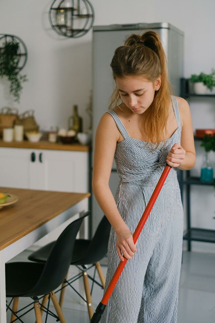 Young woman mopping kitchen floor, illustrating personal cleaning rules.