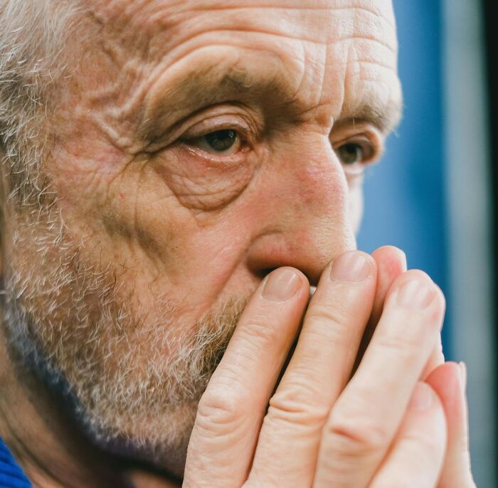 Elderly man looking concerned, covering mouth with hands, evoking a sense of disgust and contemplation.