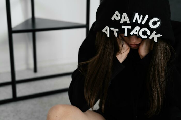 Person wearing a hoodie with panic attack text, sitting on the floor experiencing unexplainable pain and distress.