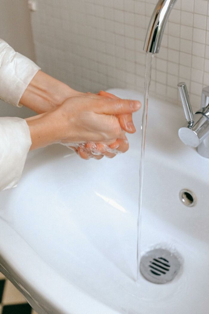 Hands washing in a sink under running water, illustrating personal cleaning rules.