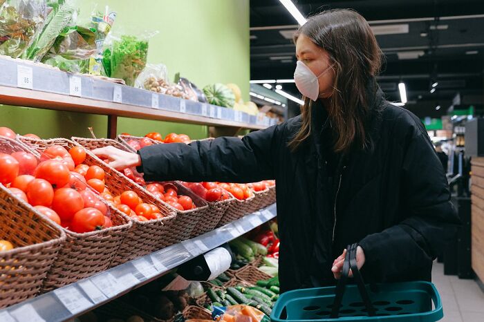 Woman wearing a mask selecting fresh vegetables in a grocery store focused on restaurant food products.