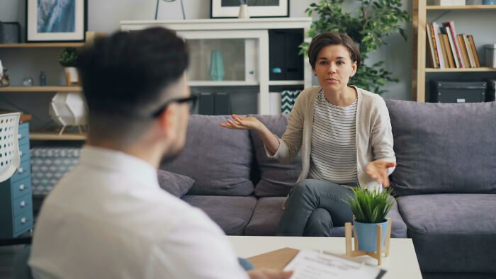 Woman sharing red pill stories in a casual living room setting, engaged in conversation with a seated man.