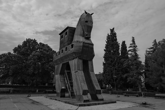 Large wooden Trojan horse sculpture standing outdoors with trees in the background representing legends quiz concept. Large wooden Trojan horse sculpture standing outdoors with trees in the background representing legends quiz concept.