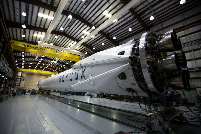 SpaceX rocket in a hangar with industrial lighting and yellow cranes overhead, showcasing engineering feats.