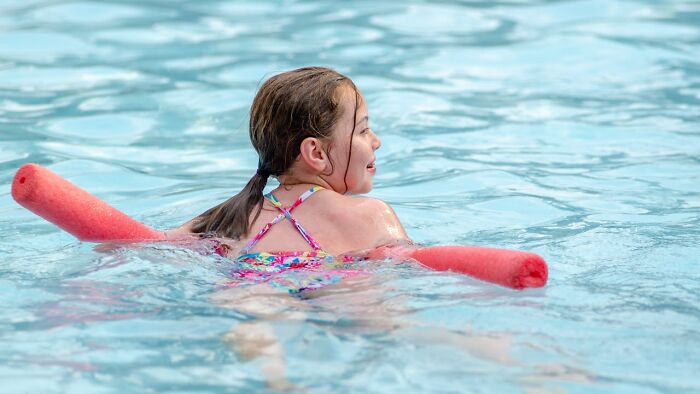 Child swimming with a red pool noodle in water, enjoying a playful moment.