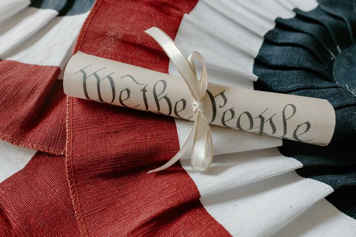 Rolled parchment titled "We the People" on an American flag-themed background.