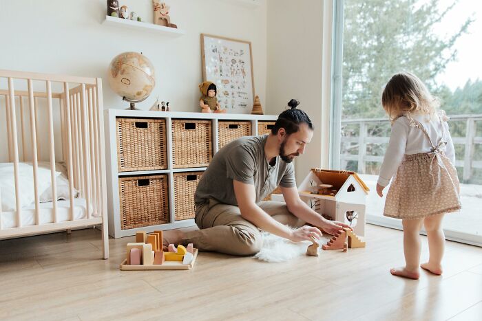 Father and daughter playing with blocks and a dollhouse, sharing a moment in a bright room with wicker storage baskets.